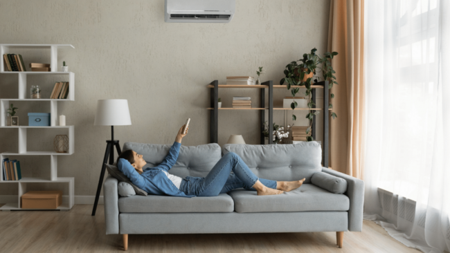Woman relaxing on couch pointing remote at AC wall unit