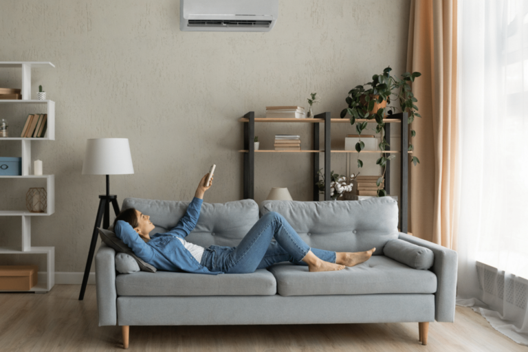 Woman relaxing on couch pointing remote at AC wall unit